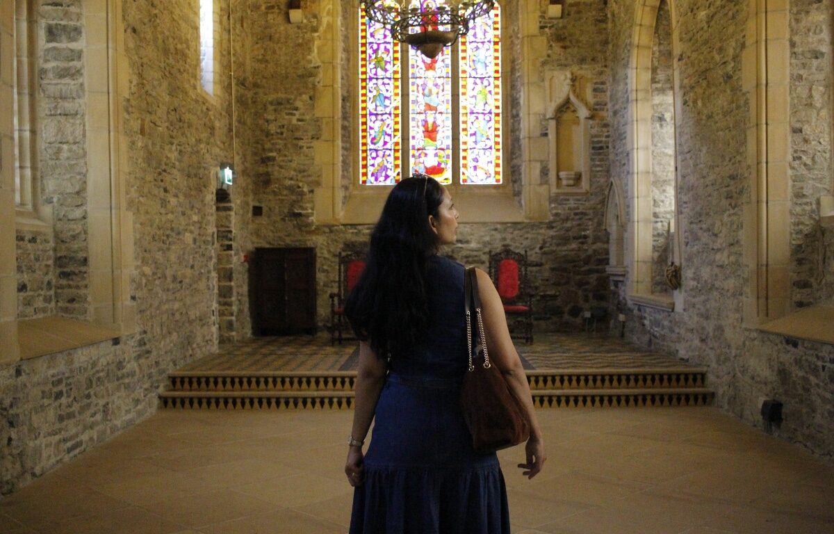 Guest admires a stunning stained-glass window in a historic hotel chapel, surrounded by stone walls and elegant lighting.