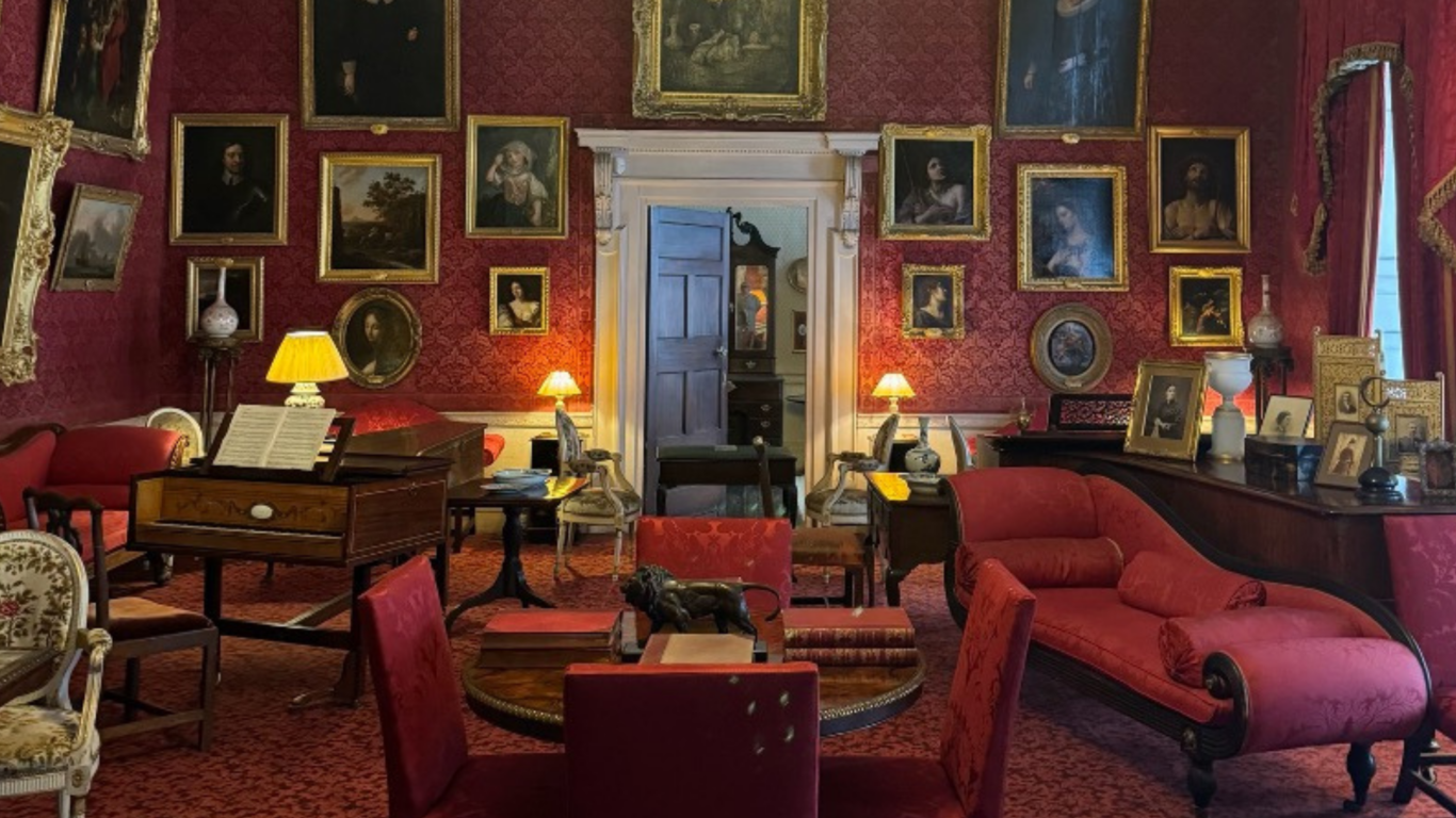Elegant drawing room with red decor, vintage furniture, and framed art, offering a cosy and luxurious ambience for guests.