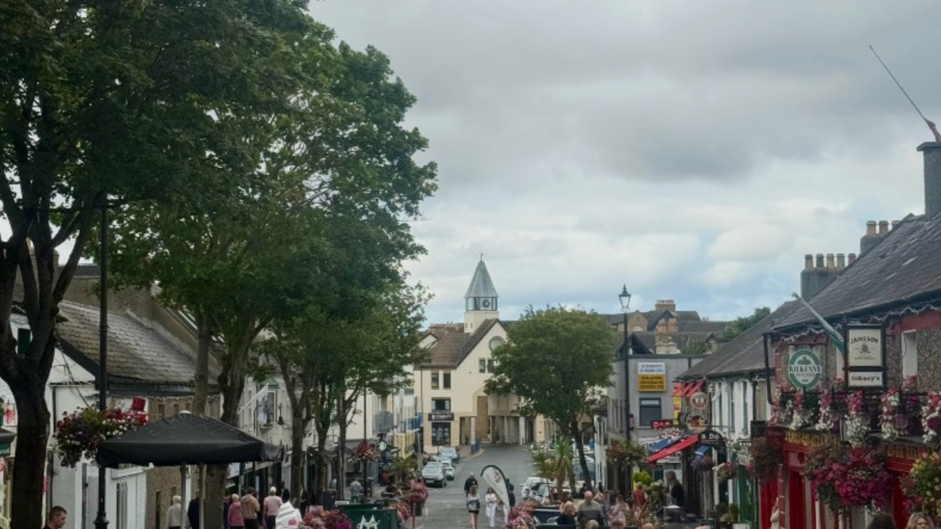 Charming street view with vibrant flowers, outdoor dining, quaint pubs, and historic architecture in a lively town centre.