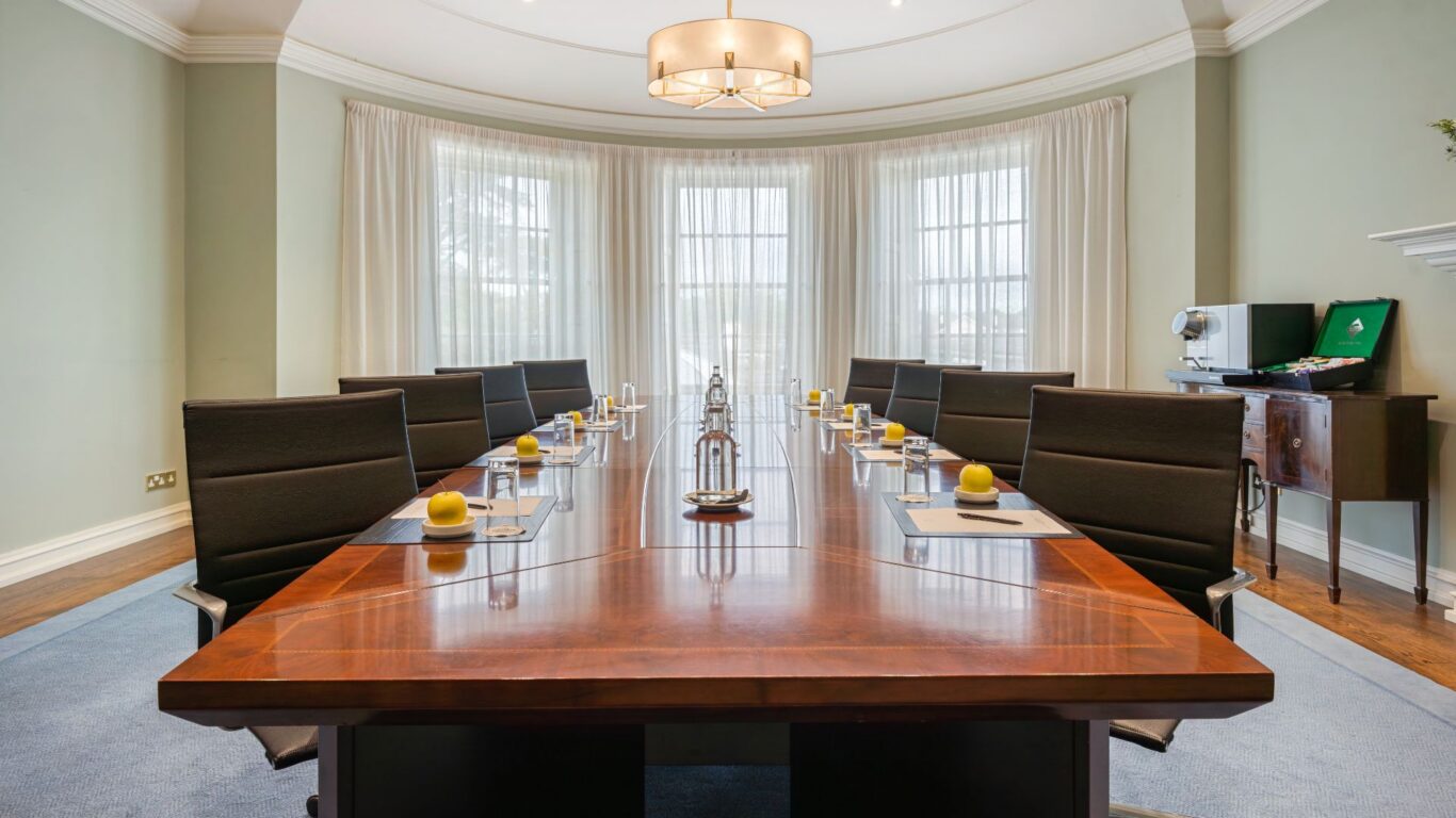 Elegant conference room with sleek wood table, plush chairs, and natural light through large windows, ideal for meetings.