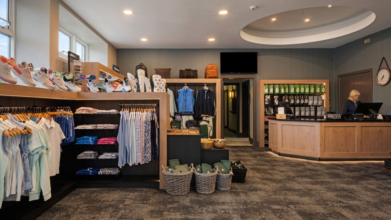 Charming hotel shop with stylish clothing, shoes, and golf gear, inviting desk for guest service. Relaxed and welcoming vibe.